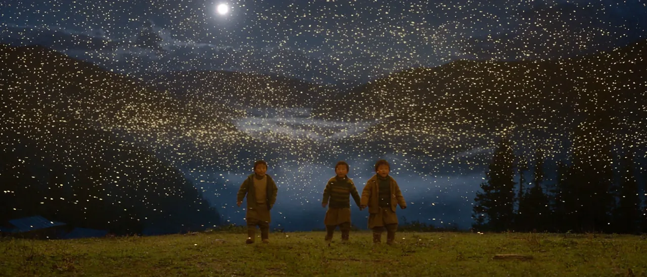 Three children standing beneath a vast swarm of fireflies on a night ridge